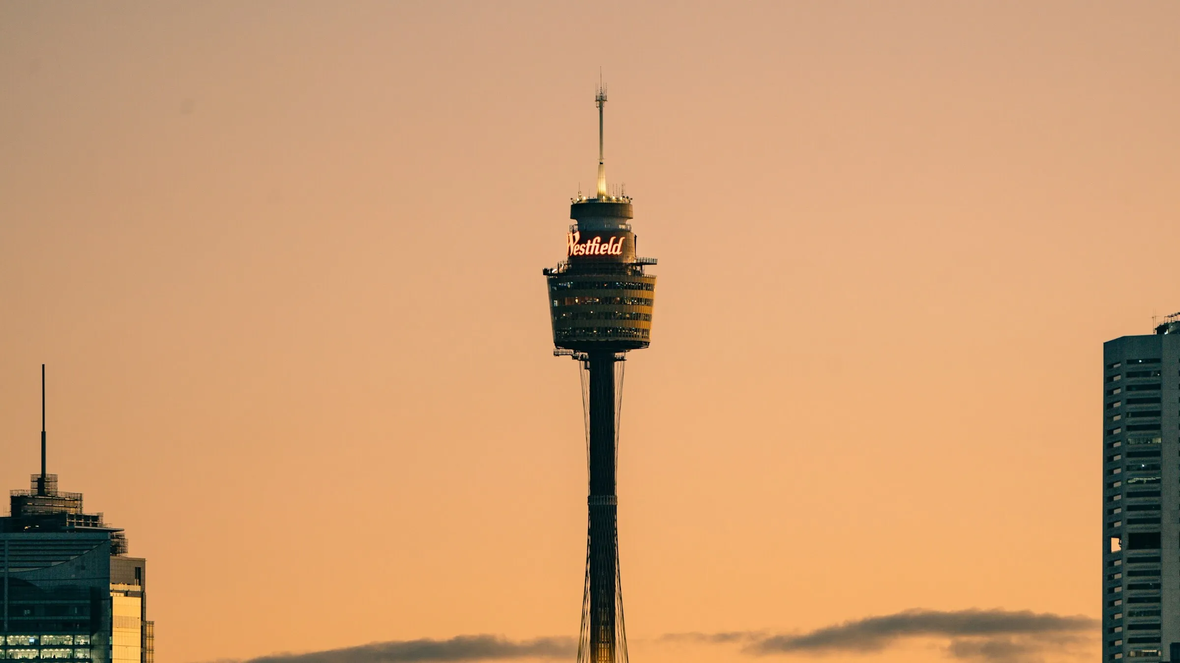 Sydney Tower with its gold turret and red Westfield sign against an orange sunset sky